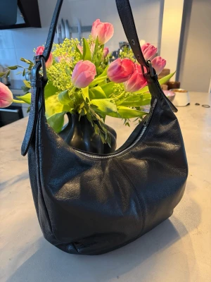 Svart axelremsväska från NUNOO - Lagom stor axelremväska från märket NUNOO. Bandet går att justera i 5 längder. Passar perfekt som vardagsväska eller skolväska.