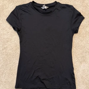 Svart basic t-shirt från H&M - En enkel svart t-shirt från H&M med rund hals och korta ärmar. Modellen är figurnära och passar perfekt till alla typer av outfits. Tillverkad i mjuk bomull för skön komfort hela dagen.