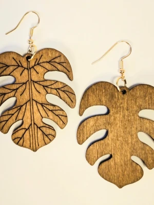 Träörhängen Monstera blad löv boho chic  - Unika örhängen i form av Monstera blad, tillverkade i ljust brunt trä med fina ingraverade detaljer på ena bladet. Krokarna är i metall med guldfinish. Perfekt för dig som gillar naturinspirerade accessoarer och vill sticka ut lite extra. Eleganta örhängen med en kombination av trä och bladmotiv.  Perfekt för att komplettera din stil med en naturlig och bohemisk touch.  Trädelen är ca 5 cm lång. Motivet är fäst på högkvalitativa örhänges-krokar i rostfritt stål.  Nya med etikett.