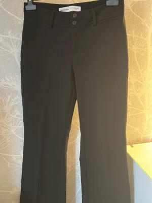 Svarta kostymbyxor från Bershka - Svarta kostymbyxor från Bershka med raka ben och mellan-hög midja. Byxorna har hällor för skärp, två knappar i midjan och diskret dragkedja. Perfekta för en clean och stilren look. Materialet känns mjukt och följsamt. 