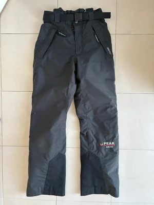 Svarta skidbyxor Peak performance stl 36/38 - Svarta skidbyxor från Peak Performance. Flera fickor med dragkedja. Förstärkta partier vid bensluten. Dam stl 36, men lite stor i storleken, mer som 38/M. Använda ett fåtal tillfällen. En defekt, litet hål vid förstärkningen, annars inget att anmärka på. Ej med axelband.