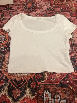 Vit ribbad croppad topp - Snygg vit croppad topp med ribbad struktur och rundad urringning. Kortärmad modell som passar perfekt till höga jeans eller kjol. Enkel och stilren design som är lätt att matcha.