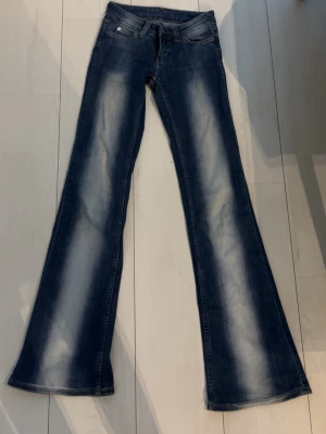 Blå bootcut jeans från cheapmonday - Säljer ett par blå bootcut jeans från cheap monday med snygga slitningar och klassisk femficksdesign. Jeansen har breda ben och låg midja, perfekt för dig som gillar en avslappnad och trendig look. Materialet är denim med tydliga blekta detaljer.