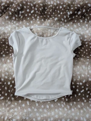 Beige croppad topp med öppen rygg - Trendig beige croppad topp med korta ärmar och snygg öppen rygg-detalj. Perfekt för dig som gillar stilrena och enkla plagg med en twist. Tunt och mjukt material som känns skönt mot huden.