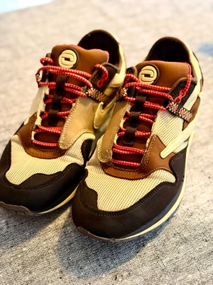 Nike Air Max 1 x Cactus Jack sneakers - Unika Nike x Cactus Jack Air Max 1 sneakers i beige, brunt och svart med röda och svarta snören. Skorna har mesh och mockadetaljer, samt Travis Scott-logga på plösen och hälen. Swoosh i vitt på sidan och coola rutiga detaljer vid snörningen.