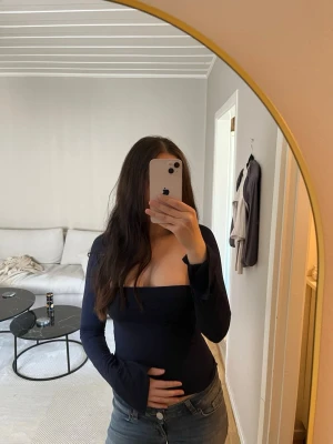 Soft Touch Square Neck Top - Snygg mörkblå offshoulder topp med lång ärm och tight passform. Perfekt för att skapa en stilren look, och den fyrkantiga ringningen ger en modern touch. Materialet känns mjukt och stretchigt, vilket gör den bekväm att bära. Endast använd fåtal gånger 