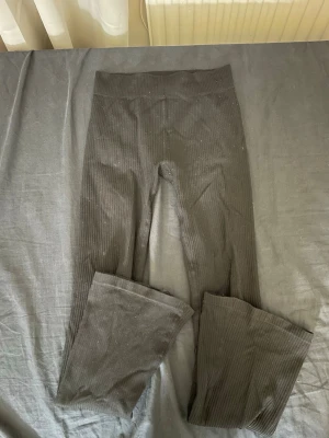 Svarta ribbade leggings med utsvängda ben - Säljer ett par svarta ribbade leggings med hög midja och utsvängda ben. De är stretchiga och bekväma, perfekta för en trendig och avslappnad look. Materialet känns mjukt och följsamt mot kroppen.