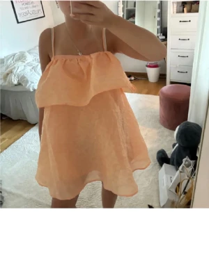 Persikofärgad volangklänning med tunna band - Supersöt kort klänning i persikofärg med volang upptill och tunna axelband. Klänningen har en luftig och flowy passform, perfekt för varma dagar. 