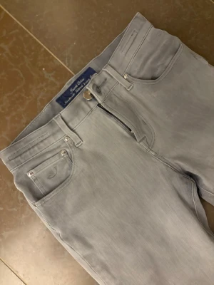 Grå jeans från Jacob Cohen - Snygga grå jeans från Jacob Cohen med klassisk femficksmodell och silverfärgade nitar. Jeansen har normal midja, raka ben och är tillverkade i mjukt denimtyg för en bekväm känsla. Perfekta för dig som gillar stilrena och tidlösa plagg.