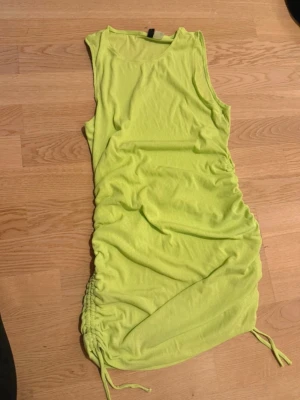 Limegrön ärmlös kortklänning - Snygg limegrön kortklänning med ärmlös design och dragsko i sidan för en cool rynkad effekt. Perfekt för dig som vill sticka ut med färg! Mjuk och stretchig känsla.