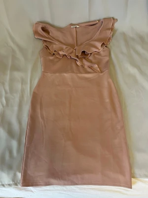 Ljusrosa klänning med volang - Söt ljusrosa klänning med volangdetaljer vid axlar och byst och urringning. Klänningen har en figurnära passform och är ärmlös, går ungefär till knäna. Storlek L. Från Nelly.