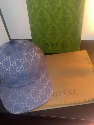 Blå GG-monogram keps från Gucci - Säljer en blå keps från Gucci med det klassiska GG-monogrammet i vitt över hela kepsen. Kepsen har justerbart spänne bak och är tillverkad i ett slitstarkt tygmaterial. Perfekt för dig som vill ha en stilren och lyxig accessoar med ikonisk design.