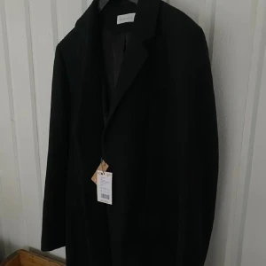 Helt ny kappa/rock herr!  - Stilren svart kappa från Pier One med klassisk krage och knäppning framtill. Kappan har diskreta fickor som är osprättade, även en innerficka. Den är helt ny, säljes pga snabb viktnedgång. Skickar fler bilder vid intresse. Djur och rökfritt hem!