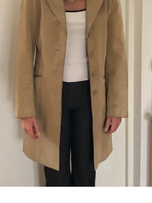 Beige mockakappa med knappar retro vintage stl M - Vintage längre mocka jacka/kappa beige mocka. Storlek M  Stilren beige kappa i mocka med klassisk krage och knäppning framtill. Lång modell med raka ärmar och diskreta fickor i sidorna. Perfekt för dig som gillar en tidlös och clean look. Ok vintage skick se bilder