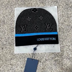 Svart mössa med blå text - Snygg svart mössa med klassiskt monogrammönster och blå rand. Märkets logga är broderad framtill i vitt. Perfekt accessoar för att lyfta din streetstyle.