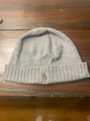 Grå stickad mössa från Polo Ralph Lauren - Detta är en Polo Ralph Lauren Signature Pony-ullmössa i ljusgrå ljung. Den verkar skonsamt använd utan synliga skador. ⭐️ Skick: 8/10 🎨 Färg: Fawn Grey Heather 📦 Snabb och försiktig frakt