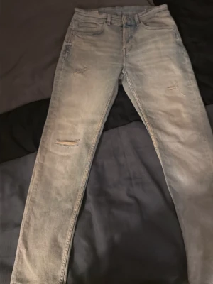 Ljusblå slitna jeans från Zara - Säljer ett par ljusblå jeans från Zara med slim fit och slitningar på benen för en trendig look. Jeansen har klassisk femficksdesign, bälteshällor och dragkedjegylf. Perfekta för dig som gillar en avslappnad men ändå stilsäker stil.