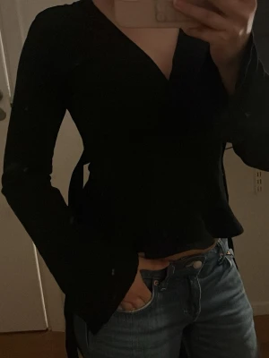 Svart långärmad v-ringad topp - Snygg svart långärmad topp med v-ringning och figurnära passform. Från Gina tricot storlek xs. Har knytband som kan knytas på sidan fram eller bak! Knappt använd.