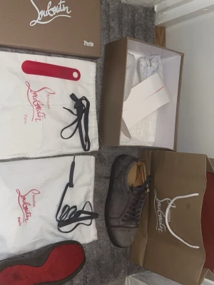 Gråa Louboutin sneakers med röd sula - Snygga gråa sneakers från Christian Louboutin med klassisk röd sula. Skorna är låga och har ovandel i mocka med matchande gråa skosnören. Kommer med , dustbags, extra skosnören och skohorn. Perfekta för dig som vill sticka ut med exklusiva detaljer. Några skavanker vid hälkappan på insidan som har förekommit vid användning men annars riktigt fina skor o bra skick!😊 Tveka inte på att ställa en fråga eller två🙏