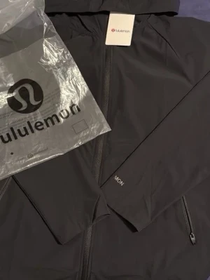Svart träningsset från Lululemon - Säljer ett svart träningsset från Lululemon med zip-jacka och matchande byxor. Setet har en modern passform, jackan har huva och dragkedja, och byxorna är smala med resår vid anklarna. Perfekt för gymmet eller sportaktiviteter.