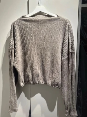 Beige ribbad croppad tröja - Säljer en beige croppad tröja med ribbad struktur och diskret mönster. Tröjan har långa ärmar och en lös passform, perfekt för en avslappnad stil. Materialet känns mjukt och lätt, vilket gör den skön att bära.