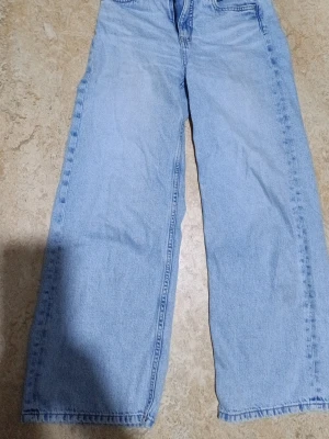 Ljusblå raka jeans från Kappahl - Säljer ett par ljusblå jeans från Kappahl i storlek 152. Jeansen har rak passform och klassisk femficksdesign. Tillverkade i denim med snygga sömmar och en avslappnad look. Perfekta för dig som gillar en enkel och tidlös stil.