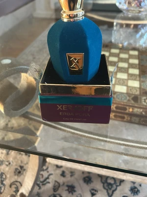 Xerjoff Erba Pura Eau de Parfum - Lyxig parfym från Xerjoff, Erba Pura, i en elegant blå flaska med sammetsliknande yta och gulddetaljer. Flaskan har en unik form och levereras i en exklusiv ask med guld- och turkosa inslag. Perfekt för dig som gillar exklusiva dofter och snygg design.