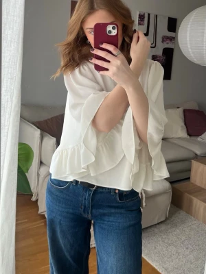 Vit blus med volangärmar - Snygg vit blus med breda volangärmar och lös passform. Blusen har rund halsringning och är tillverkad i ett lätt, flowigt material som ger en elegant look. Perfekt att matcha med jeans eller kjol för en trendig stil.