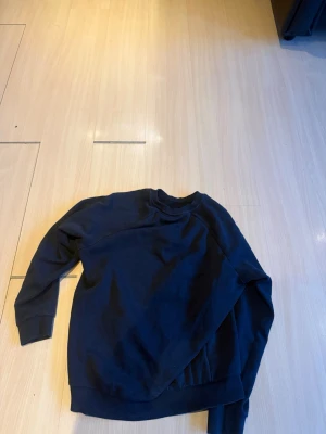 Svart sweatshirt från Peak Performance - Säljer en svart sweatshirt från Peak Performance med klassisk rund hals och diskret logga på bröstet. Tröjan har långa ärmar och ribbade muddar vid ärmslut och nederkant. Perfekt för en avslappnad och stilren look.