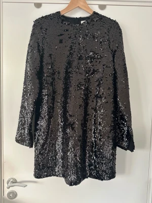 Svart Arket paljettklänning med långa ärmar - Otroligt snygg svart klänning från Arket med paljetter, i storlek 38 / M. Klassisk modell med långa ärmar med slits, rund halsringning och fin dold dragkedja bak. Stilren klassiker som funkar i alla säsonger. Mycket gott skick, som ny! Nypris 1390:-.  Skickas mot porto, kan även hämtas i Stockholm. 