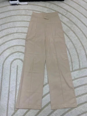 Beiga vida kostymbyxor med hög midja - Stilrena beiga kostymbyxor med hög midja och vida ben. Byxorna har pressveck framtill och stängs med knapp och dragkedja. Perfekta för en clean och trendig look. Materialet känns mjukt och följsamt.