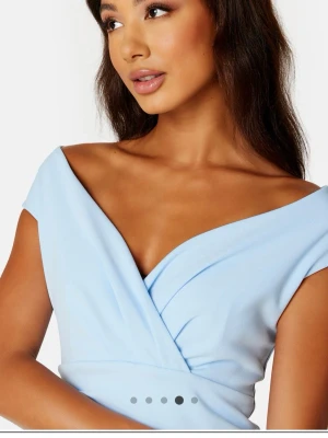 Ljusblå omlottklänning med v-ringning - Snygg ljusblå klänning med omlott-design och v-ringad hals. Klänningen har offshoulder-ärmar och smickrande drapering över midjan. Perfekt för dig som vill ha en elegant och modern look.