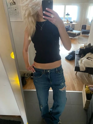 Blå slitna baggy jeans - Säljer ett par blå baggy jeans med slitningar och hål på benen. Jeansen har fem fickor, hög midja och raka ben. Perfekta för en avslappnad och trendig look. Klassisk denim med coola detaljer.