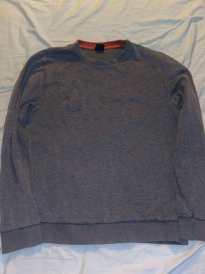 Grå sweatshirt från Hugo Boss - Snygg grå sweatshirt från Hugo Boss med diskret logga på bröstet. Tröjan har rund halsringning, ribbade muddar och en slim fit passform. Perfekt för en avslappnad men stilren look.