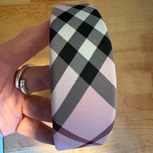 Rosa rutigt diadem i tyg - Snyggt brett diadem i rosa tyg med klassiskt rutigt mönster i svart, vitt, grått och vinrött. Liknar ett känt märke. Aldrig använt.