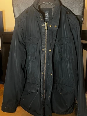 Snygg svart jacka från J. Lindbergh - Snygg svart jacka från J. Lindbergh, med flera fickor framtill, hög krage och dragkedja med tryckknappar. Jackan har långa ärmar och quiltat innerfoder för extra värme. Perfekt för kyligare dagar och har en klassisk, stilren look. Passar till vår/sommar/höst. Nypris: 4300kr, (den säljs inte längre) mitt pris: 1200kr.