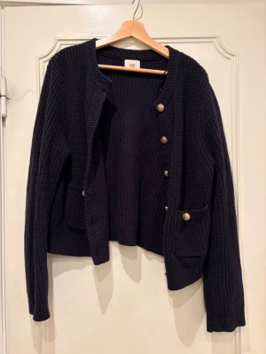 Mörkblå stickad kofta med guldknappar - Snygg mörkblå stickad kofta med rund hals, dekorativa guldknappar framtill och två fickor. Tröjan är ifrån HM i storlek EUR S men sitter lite oversized. Extremt mjuk och skön, kliar inte alls och använd bara 1 gång. 