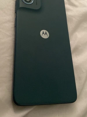 Svart Motorola Android-telefon - Säljer en blå Motorola  med stilren design och stor skärm. Baksidan har Motorola-loggan och kameran sitter i övre vänstra hörnet. Telefonen har rundade hörn och en modern look, perfekt för dig som gillar enkel och snygg teknik.