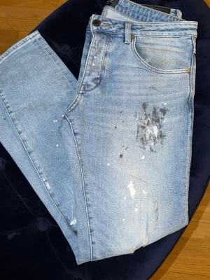 Ljusblå jeans från Neuw med färgstänk - Säljer ett par ljusblå jeans från Neuw med coola färgstänk och slitningar framtill. Klassisk femficksmodell med raka ben och normal midja. 31/32 