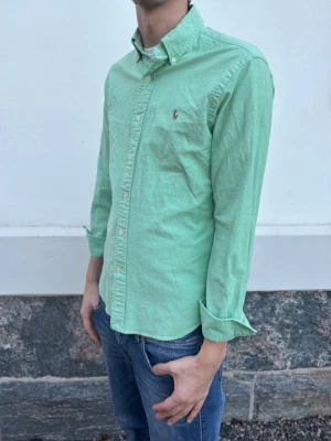 Ralph Lauren skjorta - Snygg grön skjorta från Ralph Lauren med klassisk button-down krage och broderad logga på bröstet. Skjortan har långa ärmar, knappar framtill och är tillverkad i mjuk bomull. Perfekt för en clean och stilren look.