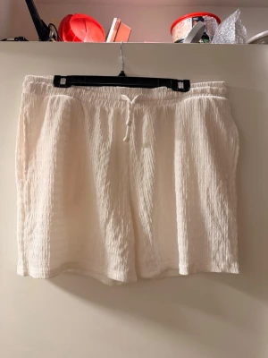 Vita crinkle-shorts med snörning - Säljer ett par vita shorts i crinkle-tyg med avslappnad passform och snörning i midjan. Perfekta för sommaren och riktigt sköna att bära. Elastisk midja för extra komfort och enkel stil.