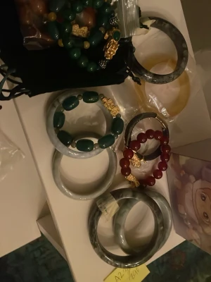 Mixade jade- och pärlarmband - Säljer flera armband i jade och pärlor. Flera av armbanden är i grön, röd och gul nyans med inslag av guldfärgade detaljer. Några är massiva bangles i grågrön jade, andra har pärlor och dekorativa detaljer. Perfekt för dig som gillar unika accessoarer. Äkta jade från Burma halsband i äkta silver med buddha kommer in och guld senare . Äkta jade ringar finns med olika nyanser , dom som intresserade skicka pm 