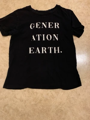 Svart t-shirt med texttryck - Cool svart t-shirt med vit text 'GENERATION EARTH.' på framsidan. Klassisk rund halsringning och korta ärmar. Perfekt till jeans eller shorts för en avslappnad look.