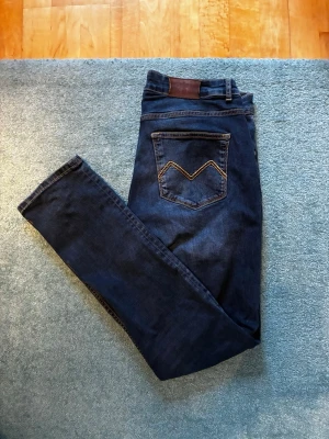 Mörkblå Morris Jeans - Storlek W32 L32. Snygga mörkblå morris slim fit jeans med klassisk femficksdesign och slitningar på knät. Jeansen  är tillverkade i ett stretchigt denimtyg för skön passform!