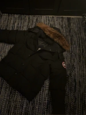 Canada Goose wyndham - Säljer en svart pufferjacka från Canada Goose med huva och klassisk logga på ärmen. Jackan har dragkedja och knappar framtill, stora fickor och en riktigt fluffig look. Perfekt för kalla dagar och riktigt snygg till alla outfits. Kan bytas emot loubs Ralph lauren puffer jacka fraktar samma dag passar M pälsen finns det är en parka den ska vara stor