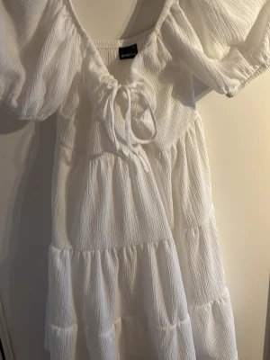Vit omlottklänning med puffärm Gina Tricot - Supersöt vit klänning från Gina Tricot med puffärmar och omlottdesign. Klänningen har knyt framtill, volangdetaljer och är tillverkad i ett lätt, strukturerat tyg. Perfekt för sommarens alla tillfällen! Lite genomskinlig men ses knappt. Använd 1-2 gånger förra året.