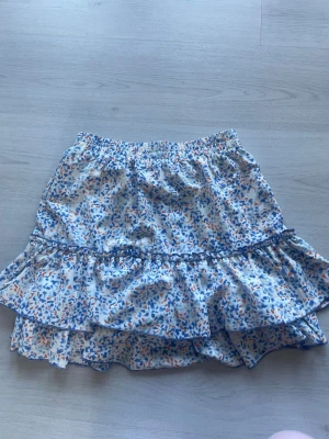 Blommig volangkjol från byClara - Supersöt kort kjol från byClara! Kjolen är jätte fin med att vila ner ifall man vill ha mer låg midjat!