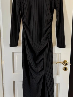 Svart ribbad långklänning från SHEIN - Snygg svart långklänning från SHEIN med ribbad struktur och långa ärmar. Klänningen har en smickrande passform och en diskret slits framtill. Perfekt för dig som gillar stilrena och trendiga plagg.