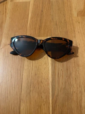 Bruna cat eye solglasögon leopardmönster Glitter - Snygga cat eye solglasögon med leopardmönstrad båge i bruna och svarta toner. Glasen är mörka och bågarna har en cool, markerad form som ger en trendig look. Perfekta för att lyfta vilken outfit som helst.