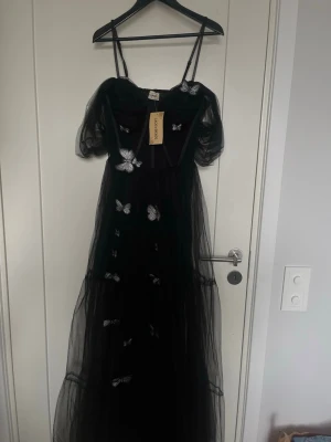 Svart bal klänning - Magisk svart långklänning från Lace and beads med tunna axelband och puffiga korta ärmar i transparent tyll. Klänningen har broderade vita fjärilar som dekoration och är perfekt för bal, bröllop eller annat event! Obs Nypris 1200 och slutsåld